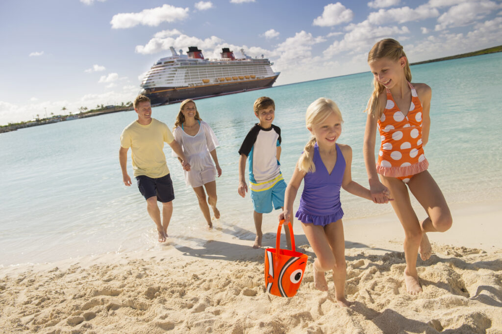 A smiling and relaxed family walks on the beach at Disney's Castaway Cay while the Disney Dream is docked behind them in the turquoise waters.